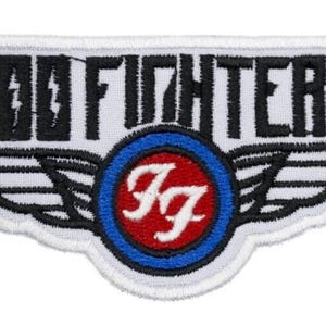 Pode incluir: Patch bordado com o texto "FOO FIGHTERS" acima de um emblema circular com as letras "FF" e asas. O emblema é vermelho e branco, rodeado por um anel azul e asas pretas.