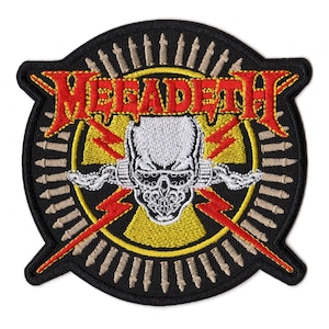 May include: A circular embroidered patch featuring the red text MEGADETH above a white skull wearing goggles. The design includes a yellow circular background, red lightning bolts, and a border of beige bullet-like shapes on a black background.