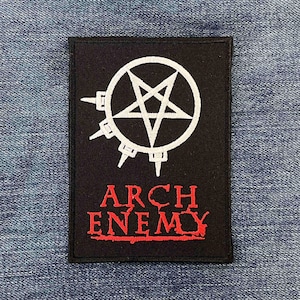 May include: A rectangular black fabric patch featuring a white embroidered pentagram symbol enclosed in a circle with four spikes extending from the left side. Below the symbol, the text ARCH ENEMY is embroidered in bold red capital letters.