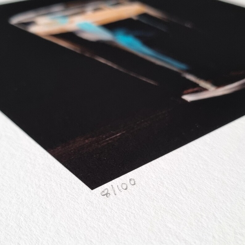 May include: A black and white print with a blurred image of a structure with blue and tan accents. The print is numbered 8/100 in the bottom right corner.