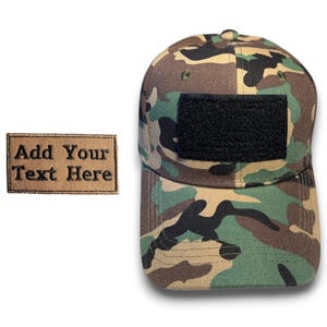 May include: Camouflage baseball cap with a black patch and a separate rectangular patch that reads "Add Your Text Here". The cap features a woodland camouflage pattern in shades of green, brown, and tan.