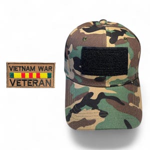 May include: Camouflage baseball cap with a black patch and a rectangular patch that reads "VIETNAM WAR VETERAN" in yellow, red, and green. The cap features a woodland camouflage pattern in shades of green, brown, and black.