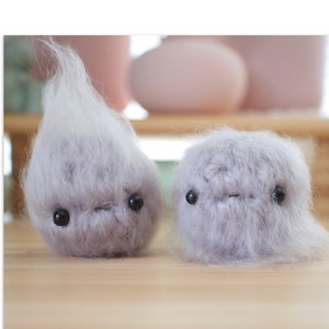 May include: Two gray fluffy crocheted stress balls with black eyes. The stress balls are on a wooden surface.