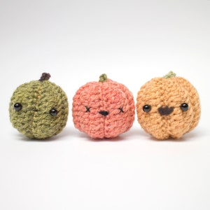 Op de afbeelding: Drie gehaakte pompoenen met verschillende gezichtsuitdrukkingen. De pompoenen zijn groen, oranje en roze.