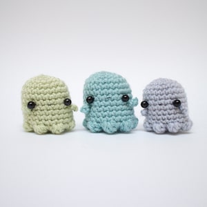 Op de afbeelding: Drie gehaakte spookvormige knuffels in groen, blauw en grijs met zwarte ogen.