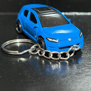 May include: A blue die-cast model car keyring. The miniature car has a black roof, black wheels, and a silver chain and keyring. The car's body is a vibrant shade of blue.