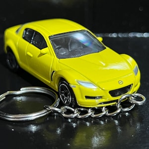 Puede incluir: Un coche de juguete amarillo brillante con ruedas negras y un llavero plateado adjunto. El coche tiene un diseño elegante con faros visibles y un interior negro. El llavero es de metal plateado.