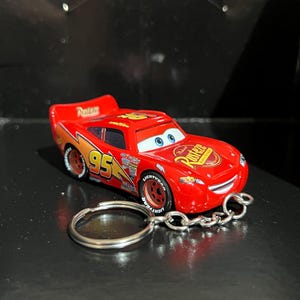 Op de afbeelding: Een rode Lightning McQueen auto sleutelhanger. De auto heeft nummer 95, bliksem graphics en het Rust-eze logo. De sleutelhanger heeft een zilveren ketting en ring.