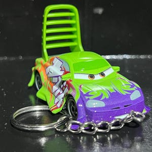 Op de afbeelding: Een gegoten speelgoedauto in groen en paars, met een opvallend ontwerp en een groene rugleuning. De auto heeft een sleutelhanger. Het ontwerp van de auto bevat oranje en witte accenten.