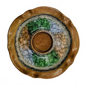 May include: A round ceramic dish with a wavy, uneven rim and a smooth, solid brown center. The surrounding ring features a textured, crystalline glaze in alternating segments of emerald green, light blue, and metallic gold, bordered by dark edges.