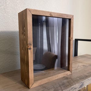 May include: A rectangular wooden display case with a clear glass front. The case is made of stained wood and sits on a wooden surface. The interior is visible through the glass.