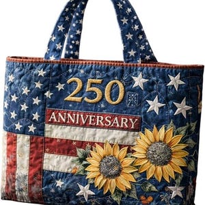 May include: A quilted tote bag featuring a patriotic American flag pattern with blue, red, and white colors. The bag displays the embroidered text 250 ANNIVERSARY in gold, accented by two large yellow sunflowers with green leaves and white stars.