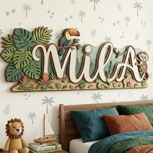 May include: A wooden wall hanging with the name "Mila" in white script, featuring a toucan, monkey, and tropical foliage. The design includes layered leaves, flowers, and a mountain scene, creating a 3D effect. The background is a light-colored wall with a palm tree pattern.