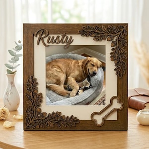Pode incluir: Uma moldura de madeira com o nome "Rusty" esculpido no topo. A moldura tem decorações de folhas de carvalho e bolotas. No interior, uma foto de um golden retriever dormindo em uma cama cinza.