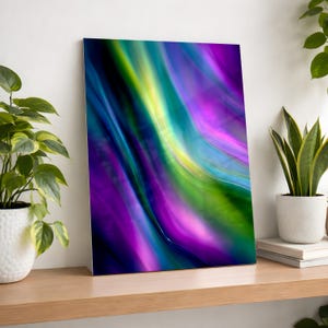 May include: Abstract art print featuring flowing, colorful waves. The artwork showcases a blend of vibrant hues, including purple, green, yellow, and blue, creating a dynamic and visually appealing composition. The print is displayed on a wooden shelf.