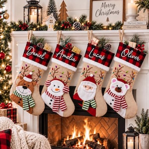 Peut inclure: Quatre chaussettes de Noël beiges avec des revers à carreaux rouges et noirs, personnalisées avec les prénoms Daniel, Amelia, Lucas et Oliver. Elles présentent des guirlandes brodées et des appliqués en peluche de renne, bonhomme de neige, Père Noël et ours polaire.
