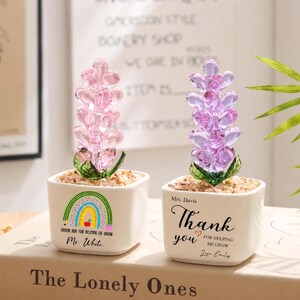 May include: Two square white ceramic planters containing glass flower sculptures. The left planter features a rainbow graphic and the text "Thank you for helping me grow" with "Mr. White." The right planter displays "Mrs. Davis Thank you for helping me grow" with "Love Emily."