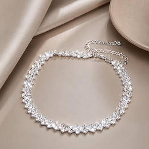 May include: A silver-toned choker necklace featuring a double row of clear, faceted, round-cut stones arranged in a zigzag pattern. The necklace includes a silver-colored metal chain extender with a small round bead at the end for adjustable length.