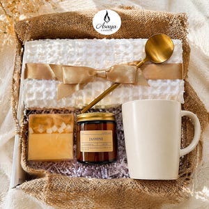 May include: A white ceramic mug with a black handle and the text "But First, Coffee" in a black, handwritten-style font. The mug is on a white surface.