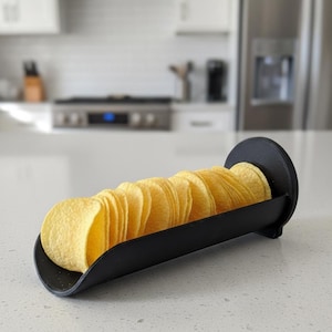 Può includere: Un porta patatine nero e curvo pieno di patatine dorate. Il supporto è realizzato in un materiale nero opaco ed è progettato per contenere le patatine. Lo sfondo è una scena di cucina sfocata.