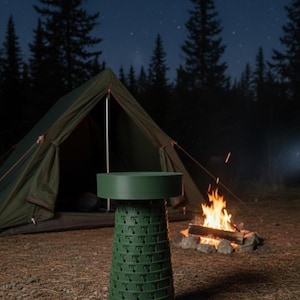 May include: A green, collapsible camping stool with a circular top and a patterned, accordion-style body. The stool is set up outdoors near a tent and campfire, under a starry night sky. The scene evokes a sense of adventure and outdoor recreation.