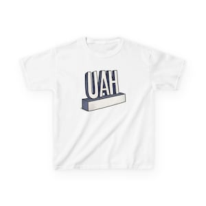 May include: White t-shirt featuring the word "UAH" in a 3D design. The letters are white with a dark blue outline, and the base is a light gray rectangle with blue shading. A casual, everyday wear tee.