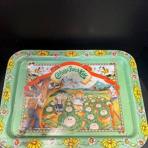 May include: A rectangular metal serving tray with a light green border featuring a yellow and white daisy pattern. The center displays a Cabbage Patch Kids illustration with characters in a garden, a tree, and the text Cabbage Patch Kids.