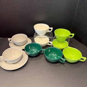 May include: A collection of eight ceramic cups and saucers in various shades of green, cream, and speckled gray. The set includes two speckled gray cups with matching saucers, two solid cream cups, two dark green cups, and two bright lime green cups.