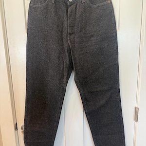 May include: High-waisted charcoal grey denim jeans featuring a button fly closure, five-pocket styling, and copper-toned metal rivets at the pocket corners. The straight-leg trousers are constructed from a dark, solid-colored cotton denim fabric.