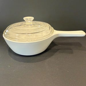 May include: A white ceramic mug with a black handle and the text "But First, Coffee" in a black, handwritten-style font. The mug is on a white surface.