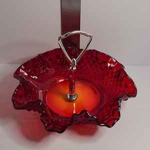 May include: A two-tiered serving dish with a red, textured glass bowl and a silver handle. The bowl has a ruffled edge and a diameter of approximately 8 inches. The dish is suitable for serving appetizers or desserts.