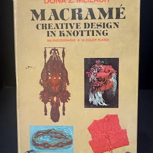 May include: A tan hardcover book titled Macramé Creative Design in Knotting by Dona Z. Meilach. The cover features black and red text, 356 photographs, 18 color plates, and three images of knotted fiber art projects in red, white, and tan tones.