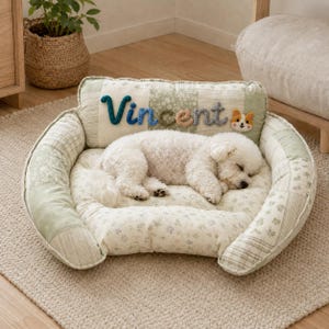 May include: A plush, rectangular pet bed featuring a patchwork design in shades of sage green, cream, and white. The backrest displays the name Vincent in colorful, raised yarn lettering alongside a small, embroidered dog face applique.