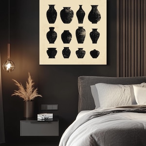 Puede incluir: Una obra de arte enmarcada con doce siluetas de jarrones negros sobre un fondo crema. Los jarrones varían en forma y tamaño, con una apariencia texturizada y desgastada. La obra se exhibe sobre una cama con ropa de cama gris, creando una estética moderna y minimalista.