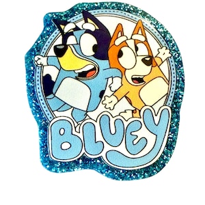 May include: A glittery blue sticker featuring the word "BLUEY" in light blue, with cartoon images of two dogs. One dog is blue, the other is orange. The sticker has a rounded, irregular shape and a white background.