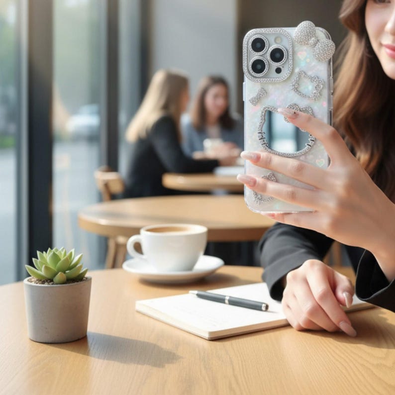 May include: A clear phone case with a decorative design featuring a bow, hearts, and a cartoon character. The case has a sparkly, iridescent finish and is embellished with rhinestones. The phone case is being held in front of a blurred background.