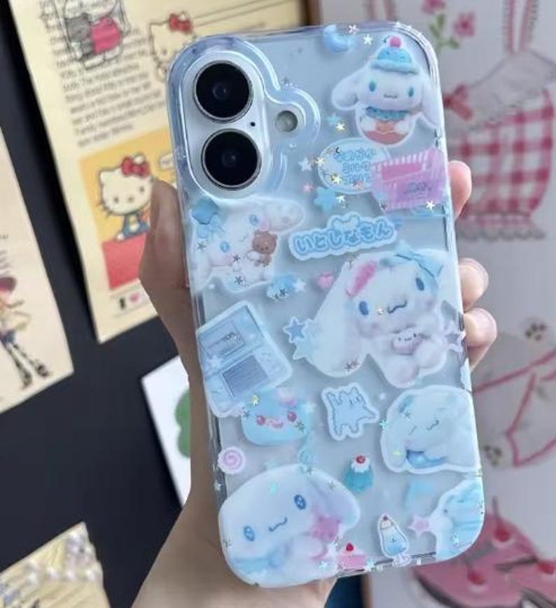 May include: Clear phone case decorated with blue and white cartoon characters and Japanese text. The case features various shapes and designs, including stars, clouds, and desserts. The case is designed to fit a smartphone.