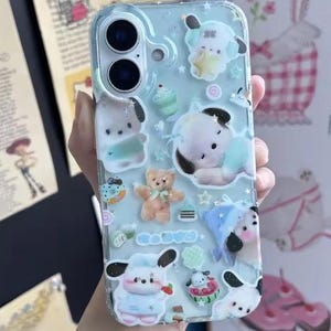 May include: A clear phone case with a light blue background, decorated with cartoon characters, stars, and small desserts. The case features a teddy bear, a cupcake, and a dog-like character. The phone case is designed to fit a smartphone.