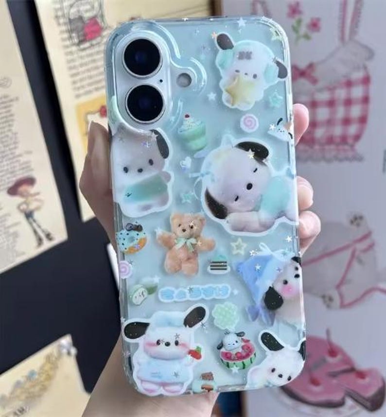 May include: A clear phone case with a light blue background, decorated with cartoon characters, stars, and small desserts. The case features a teddy bear, a cupcake, and a dog-like character. The phone case is designed to fit a smartphone.