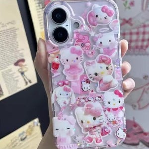 May include: Clear phone case with multiple pink Hello Kitty and other character designs. The case has a variety of 3D embellishments, including bows, dresses, and other decorative elements. The case is designed to fit a smartphone.