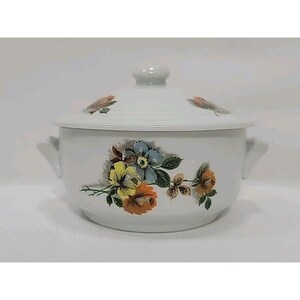 May include: White ceramic casserole dish with lid, featuring a floral design in yellow, blue, and orange. The dish has two handles and a knob on the lid. A vintage kitchenware item.