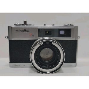 May include: A vintage Minolta 7s camera with a silver top and black body. The lens is prominent, featuring the text "ROKKOR-PF 1:1.8 f=45mm". The camera has a classic design, with dials and buttons on top.