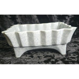 May include: A rectangular ceramic planter with a light grey crackle glaze finish. The vessel features a scalloped, wavy rim design and is supported by four short, sturdy feet at the corners, providing a raised base for the main basin structure.