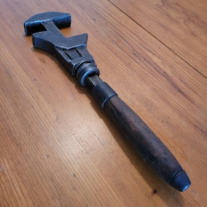 May include: A vintage adjustable spanner with a dark metal head and a wooden handle. The spanner is designed for tightening or loosening nuts and bolts. The handle is a dark brown colour.