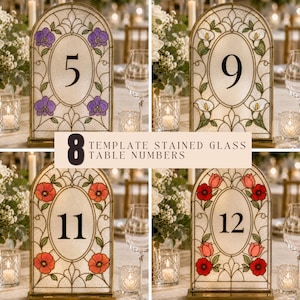 May include: Four arched stained glass table numbers featuring floral designs and black numerals. The designs include purple orchids, white calla lilies, orange poppies, and red tulips. Each piece has a central oval frame and a metal base.