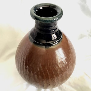 May include: A handcrafted ceramic vase with a textured, brown body and a black neck. The rim is dark green. The vase has a bulbous shape and a glossy finish, suitable for home decor.