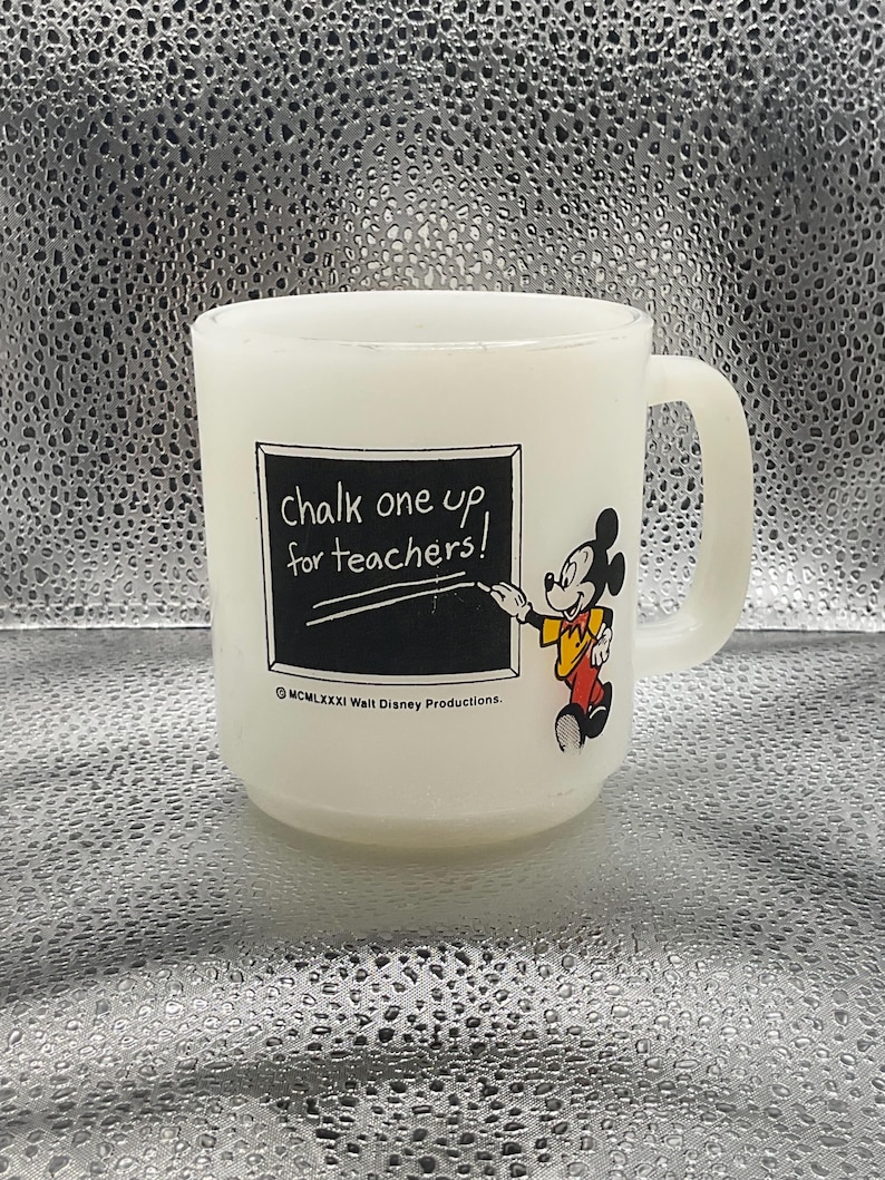 K&ouml;nnte beinhalten: Wei&szlig;er Glasbecher mit Henkel, mit Mickey Mouse und dem Schriftzug "chalk one up for teachers!". Mickey ist in seiner ikonischen Kleidung abgebildet und zeigt auf eine Tafel. Der Becher ist wahrscheinlich ein Vintage-Artikel.