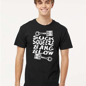 Peut inclure: T-shirt noir avec l'inscription blanche "SUCK SQUEEZE BANG BLOW" et des graphiques de pistons. Le t-shirt est de style col rond.