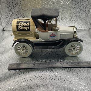 Puede incluir: Un camión de juguete vintage con techo y guardabarros negros. El camión es blanco con interior marrón y un barril en la parte trasera que dice "Food Shop". El camión tiene el logotipo de Amoco en el lateral.