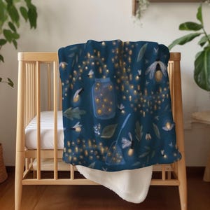 Puede incluir: Una manta azul marino con un diseño de luciérnagas, hojas y un tarro brillante. La manta está sobre una cuna de madera, mostrando un reverso blanco suave y afelpado. El diseño evoca una escena nocturna mágica.